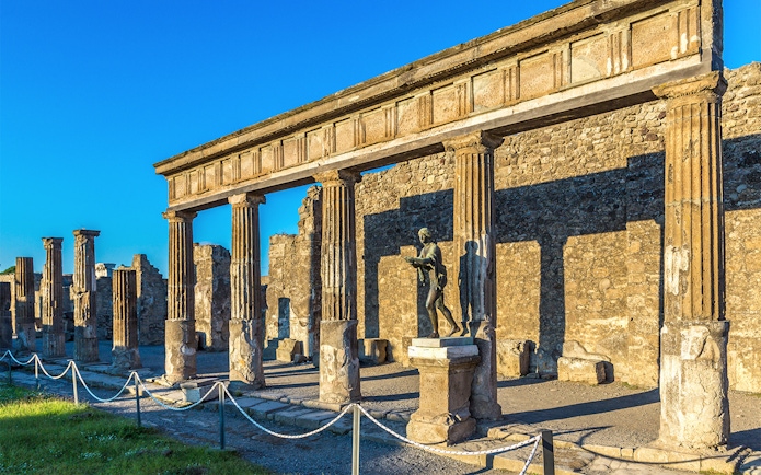 Ancient ruins and statue in Pompeii, Italy, under a clear blue sky.