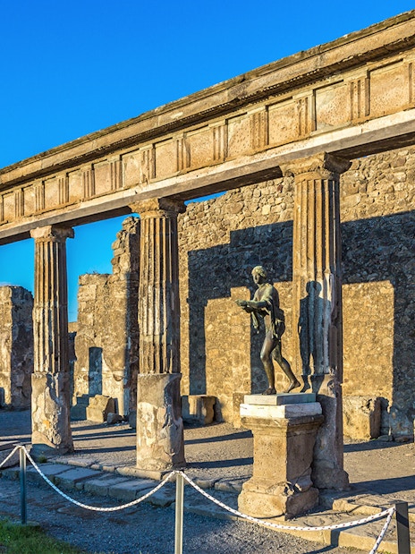 Ancient ruins and statue in Pompeii, Italy, under a clear blue sky.