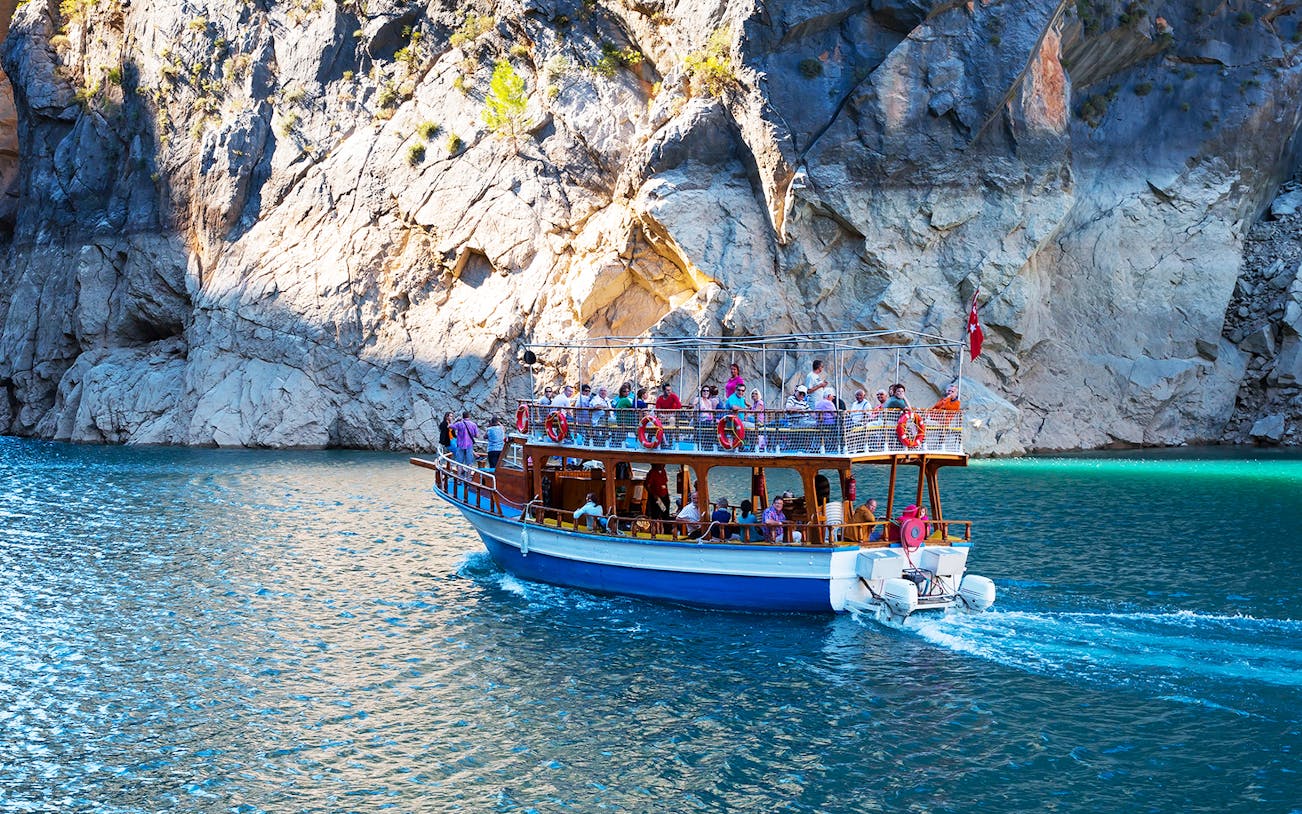 Boat tour with tourists navigating Green Canyon's rocky cliffs near Antalya.