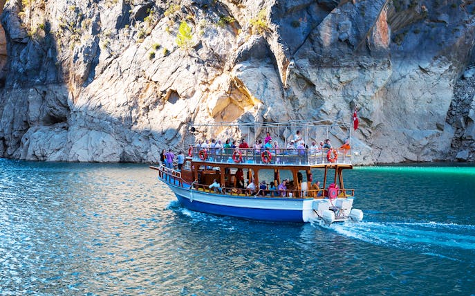 Boat tour with tourists navigating Green Canyon's rocky cliffs near Antalya.