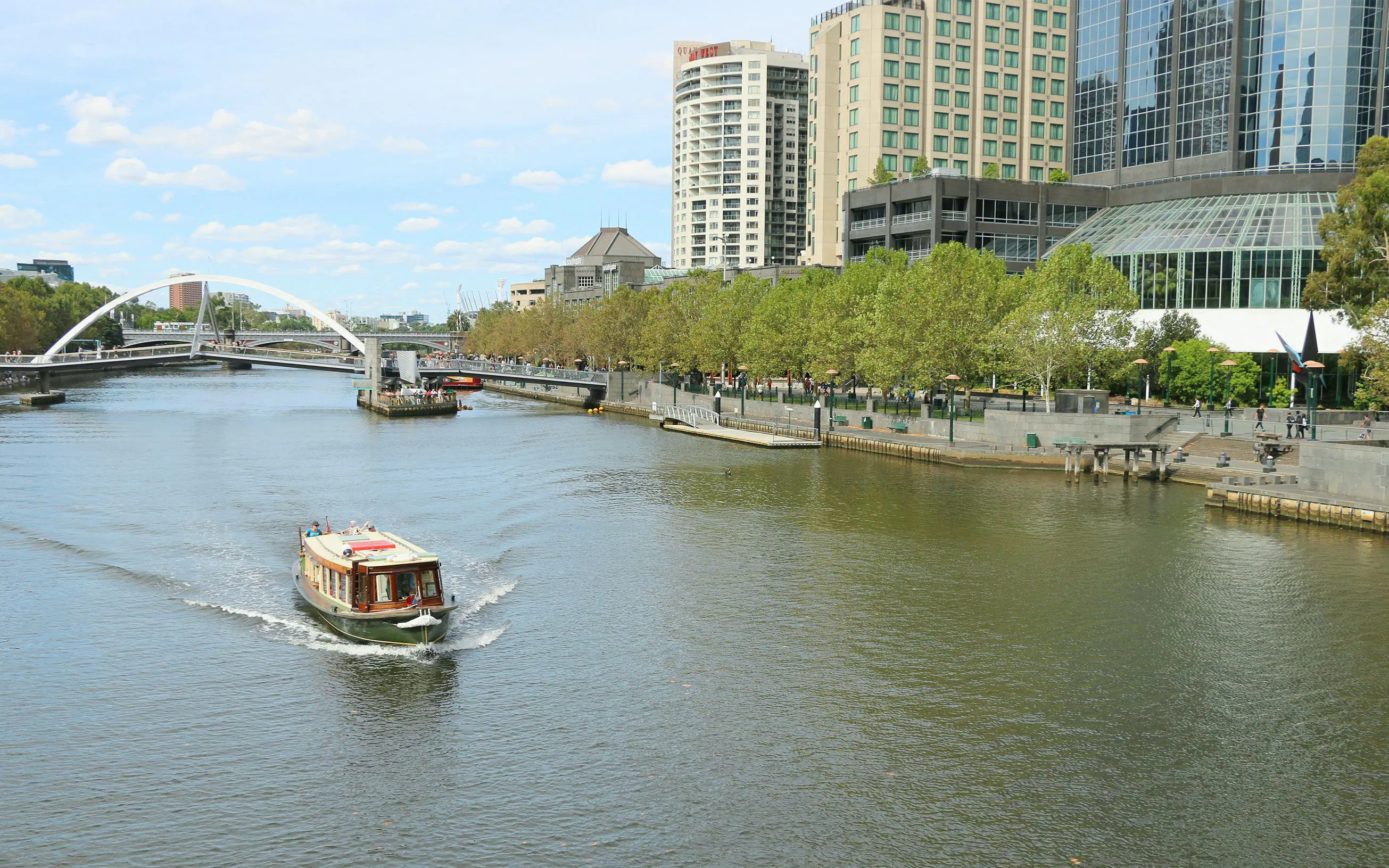 Yarra River cruise boat passing Southbank buildings and bridge in Melbourne.