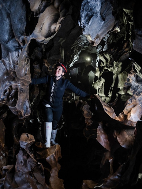 Person exploring Okohua Glowworm Cave in Waitomo, surrounded by unique rock formations.