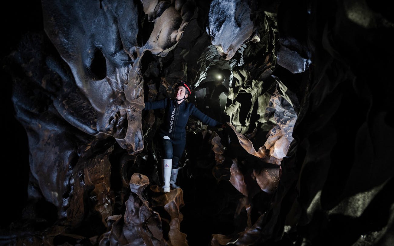 Person exploring Okohua Glowworm Cave in Waitomo, surrounded by unique rock formations.