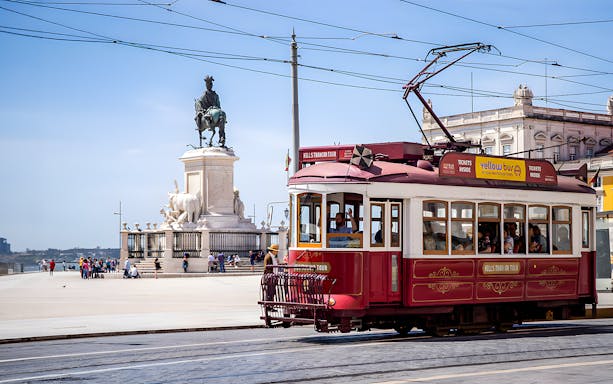 Lisbon tram passing by Praça do Comércio with equestrian statue in view.