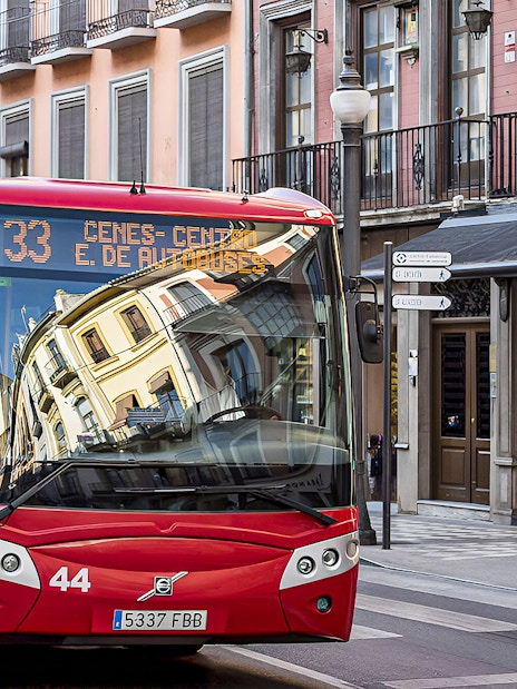 Red bus on a street in Granada, Spain, near shops and pedestrians.