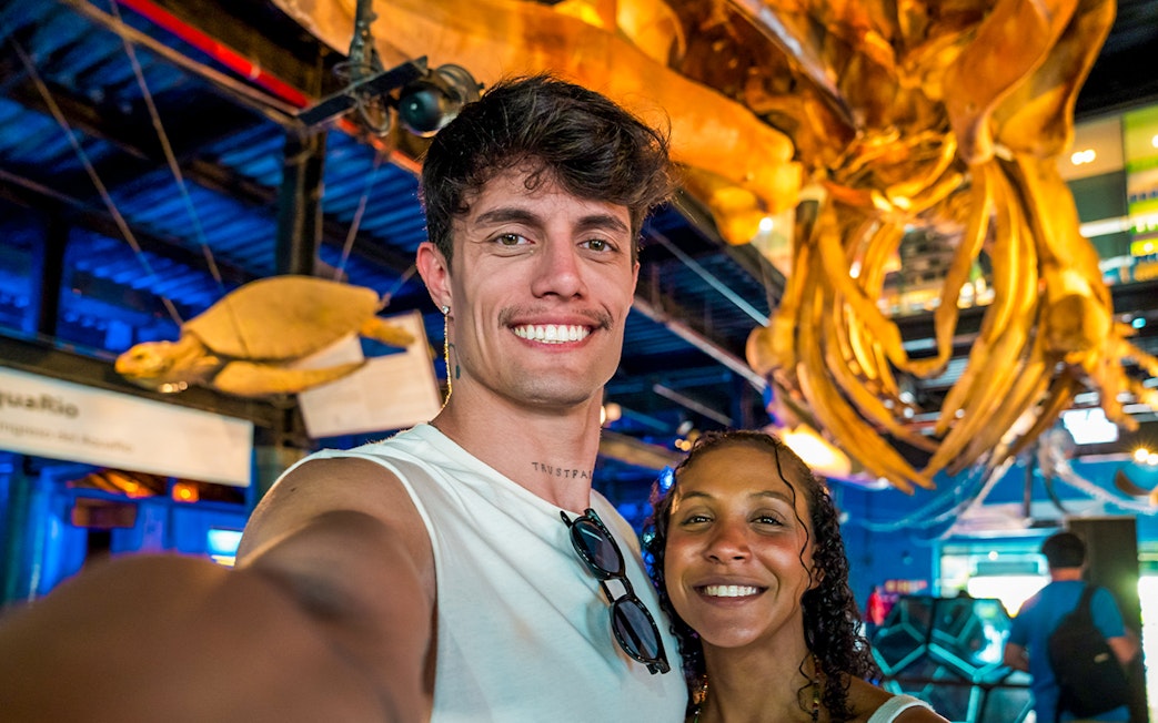 Tourists smiling in front of large octopus structure at AquaRio aquarium in Rio de Janeiro.