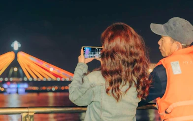 Two people on a Da Nang night motorbike tour, capturing the illuminated bridge.