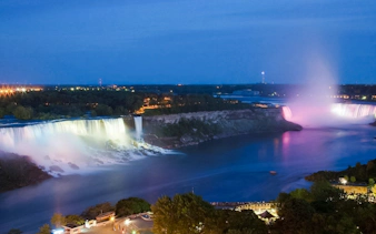 Niagara Falls USA illuminated at night with colorful lights reflecting on the water.