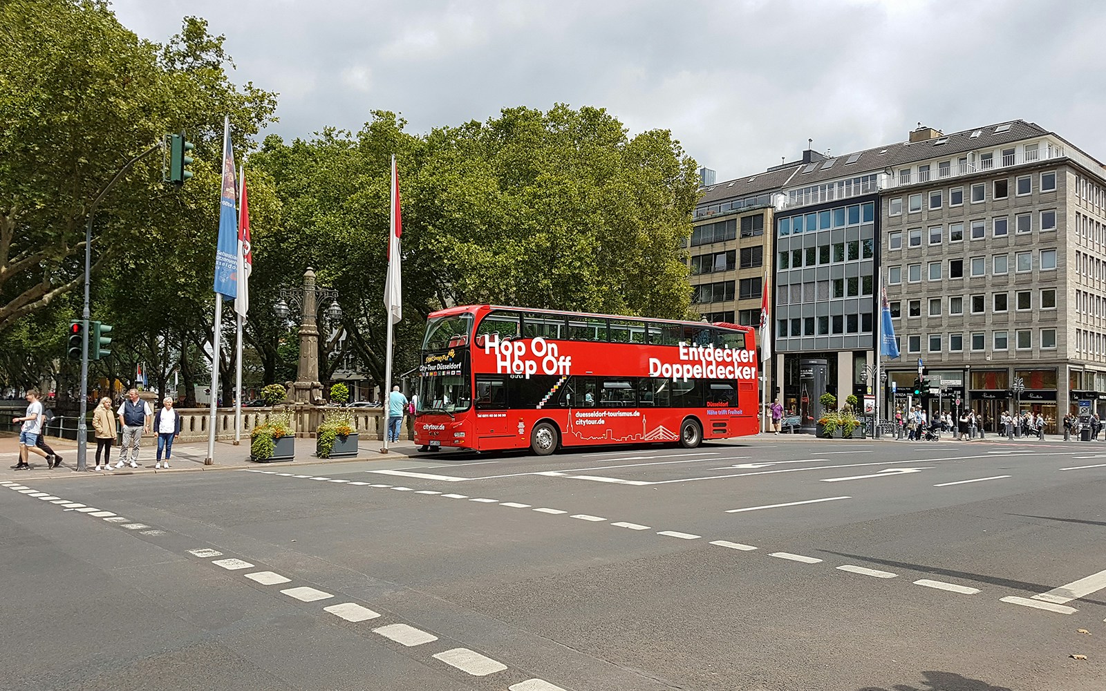 Dusseldorf hop on hop off bus at city intersection with trees and buildings.