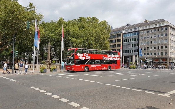 Dusseldorf hop on hop off bus at city intersection with trees and buildings.