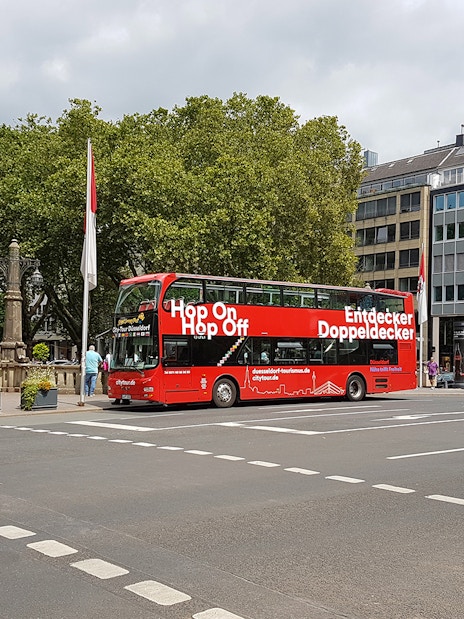 Dusseldorf hop on hop off bus at city intersection with trees and buildings.