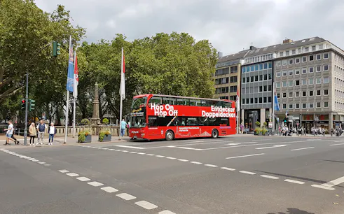 Dusseldorf hop on hop off bus at city intersection with trees and buildings.