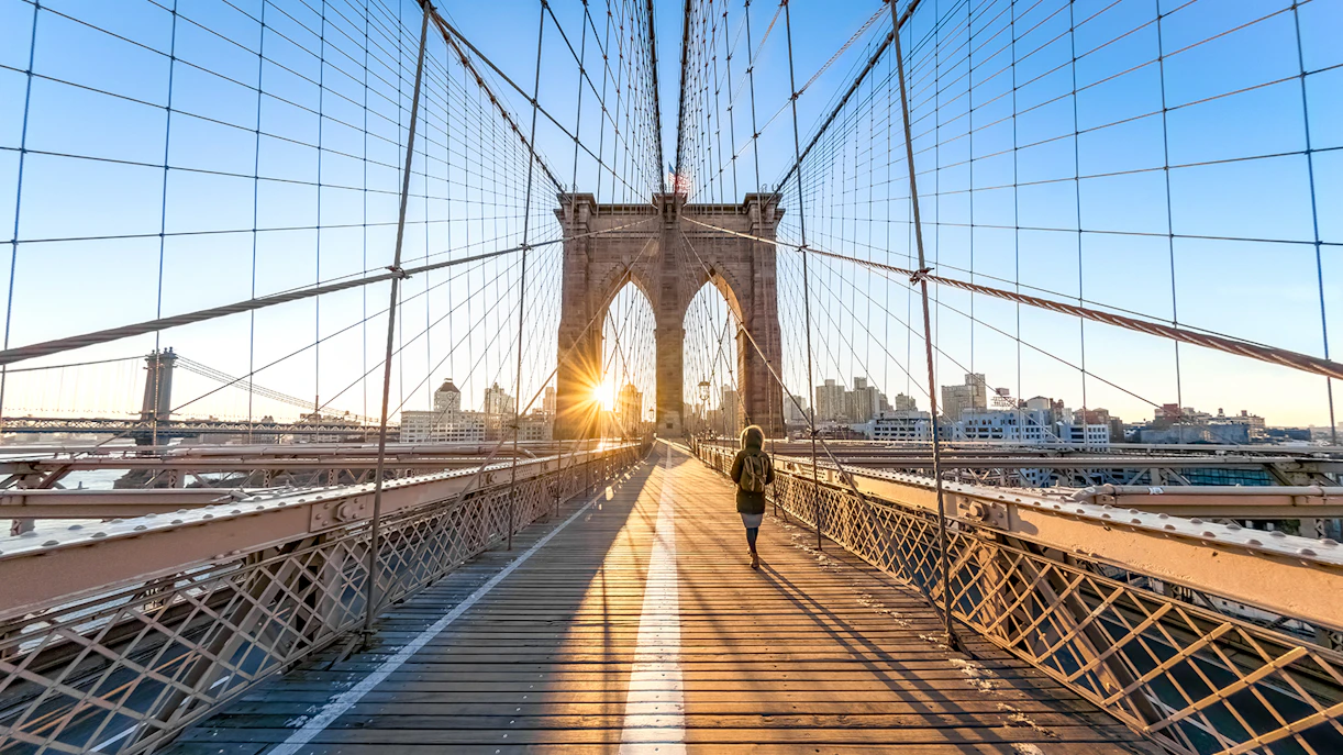 Woman walking on Brooklyn Bridge at sunrise, New York City.