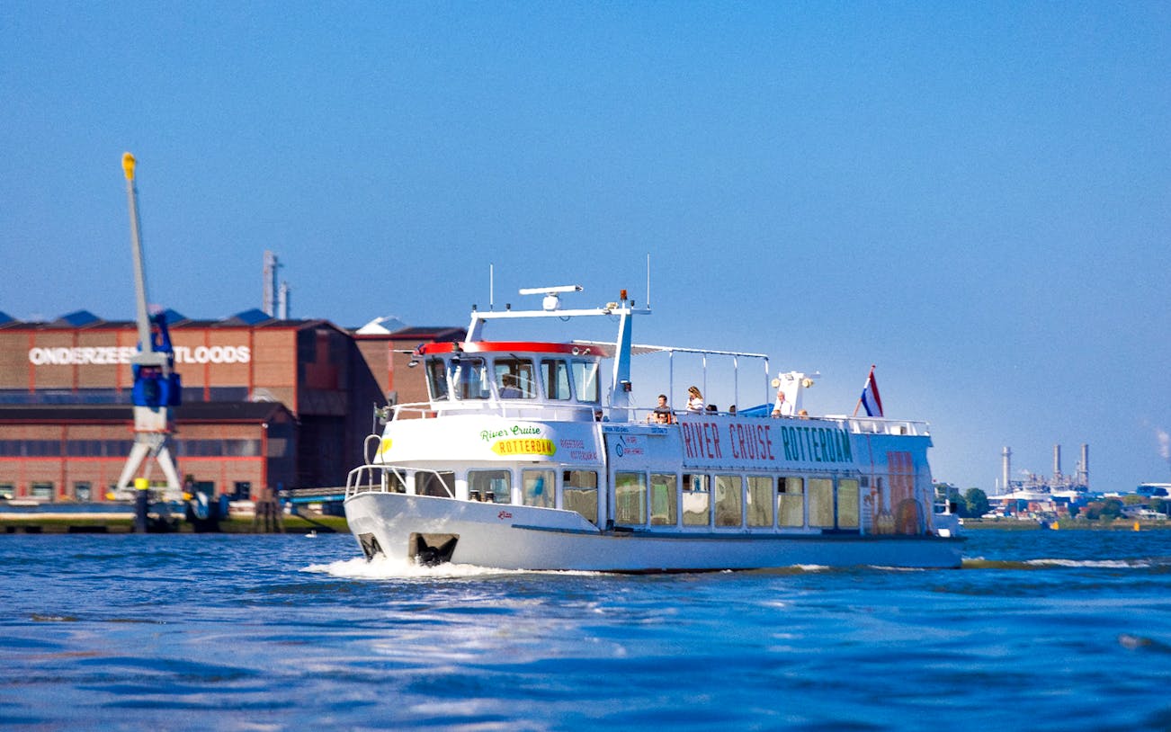 River cruise boat on Rotterdam's Maas River with city skyline in the background.