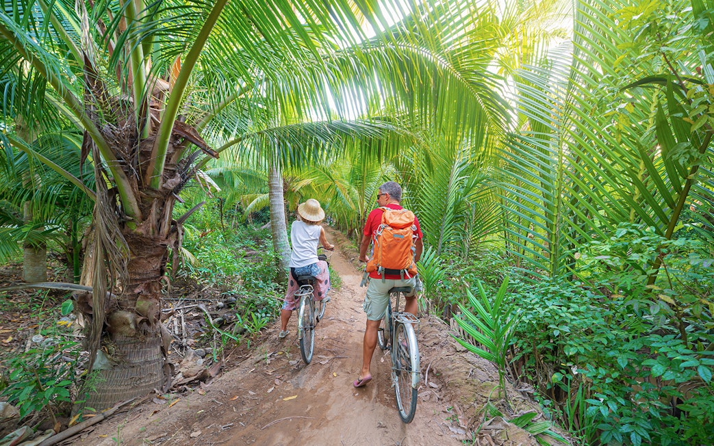 Tourists biking through lush palm trees in My Tho, Mekong Delta.