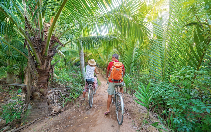 Tourists biking through lush palm trees in My Tho, Mekong Delta.