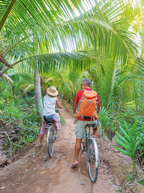Tourists biking through lush palm trees in My Tho, Mekong Delta.