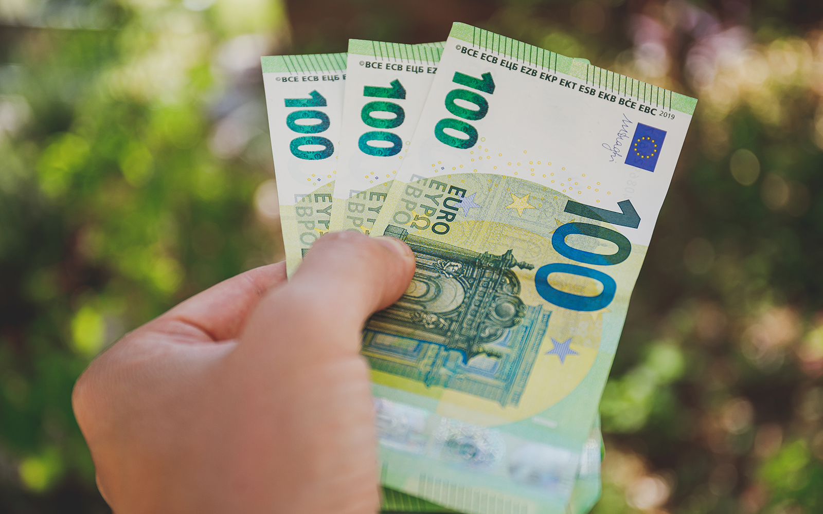 Male hand holding 100 euro banknotes on green background