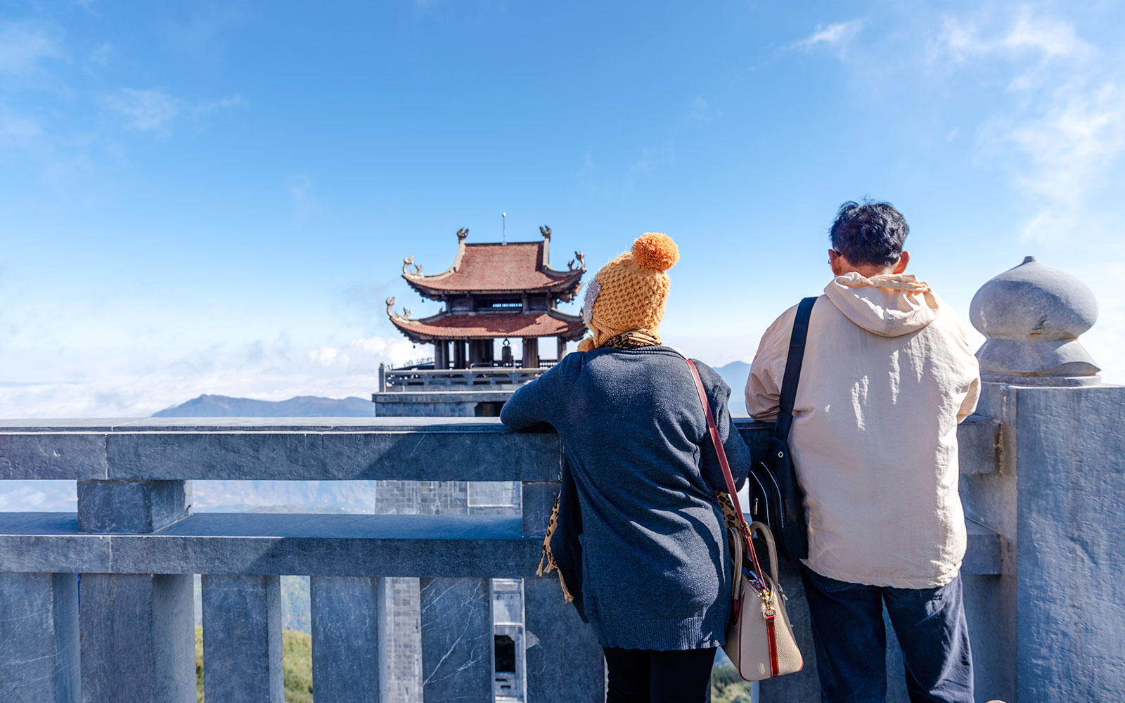 Tourists admire the view at Fansipan peak with a traditional pagoda in the background.