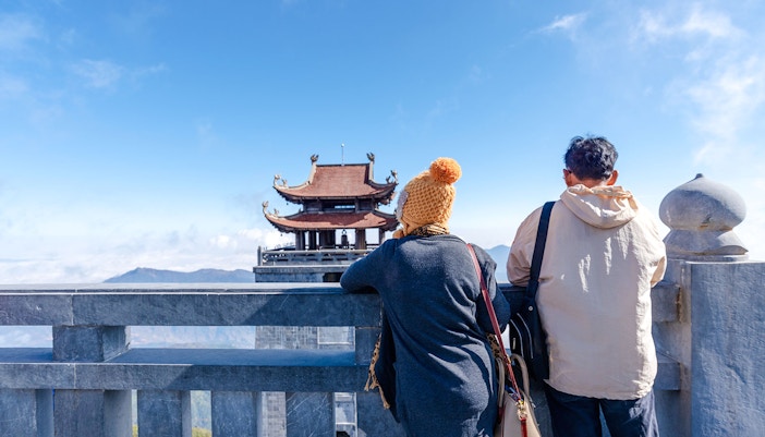 Tourists admire the view at Fansipan peak with a traditional pagoda in the background.