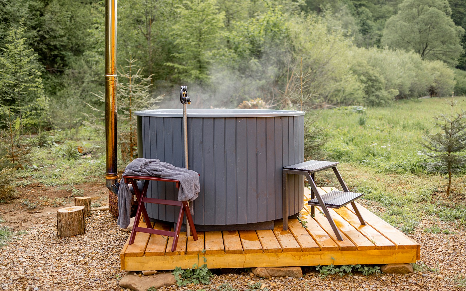 Franz Josef Waiho Hot Tub in a lush forest setting with wooden deck and steps.