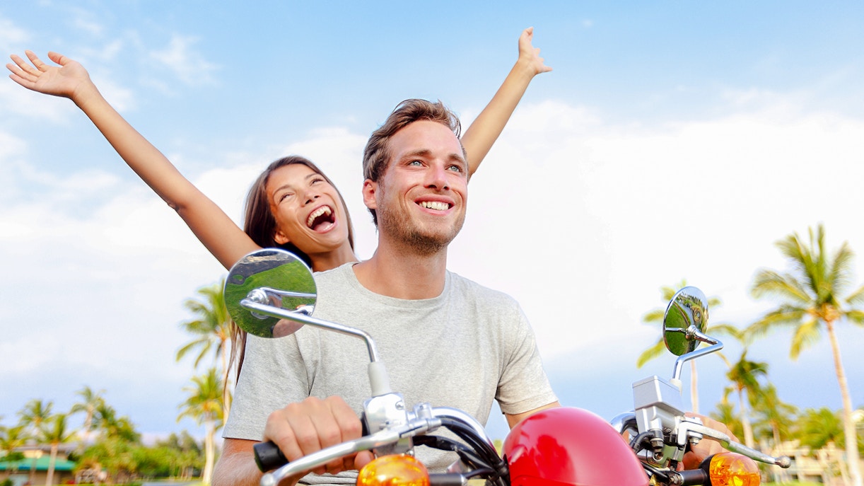 Couple riding a motorbike through palm trees in Bali.
