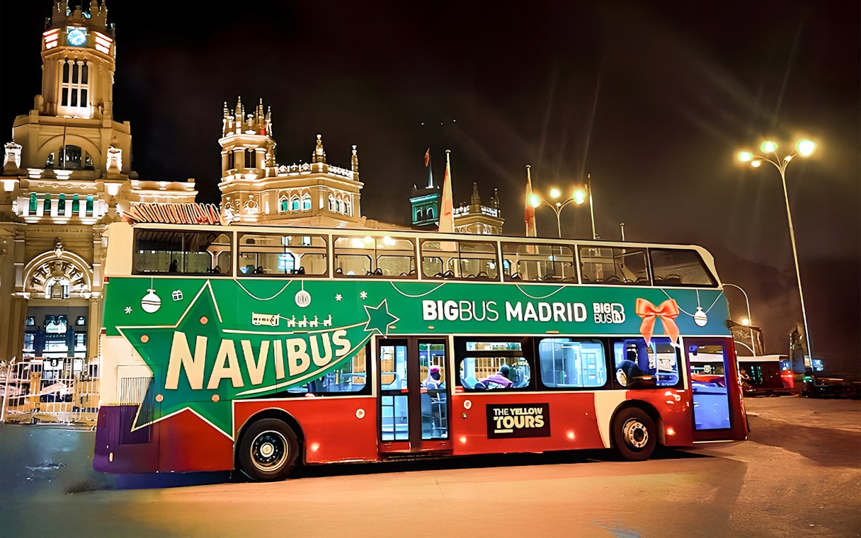 Big Bus Madrid Navibus Christmas Tour bus at night near illuminated historic building.