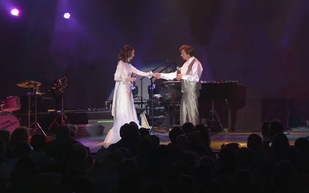 Performers on stage during Carpenters Legacy show with piano and drum set in background.