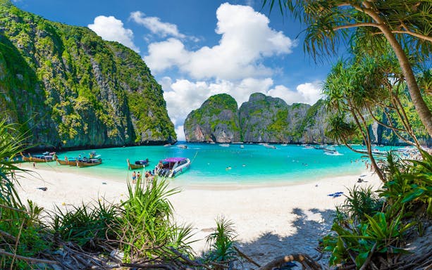 Maya Bay beach with boats and tourists, surrounded by limestone cliffs, Phuket, Thailand.