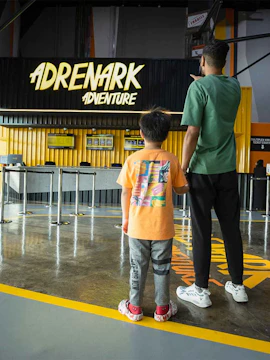 Father and child at Adrenark Theme Park entrance, pointing at the ticket counter.
