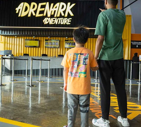 Father and child at Adrenark Theme Park entrance, pointing at the ticket counter.