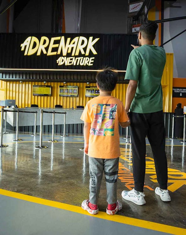 Father and child at Adrenark Theme Park entrance, pointing at the ticket counter.