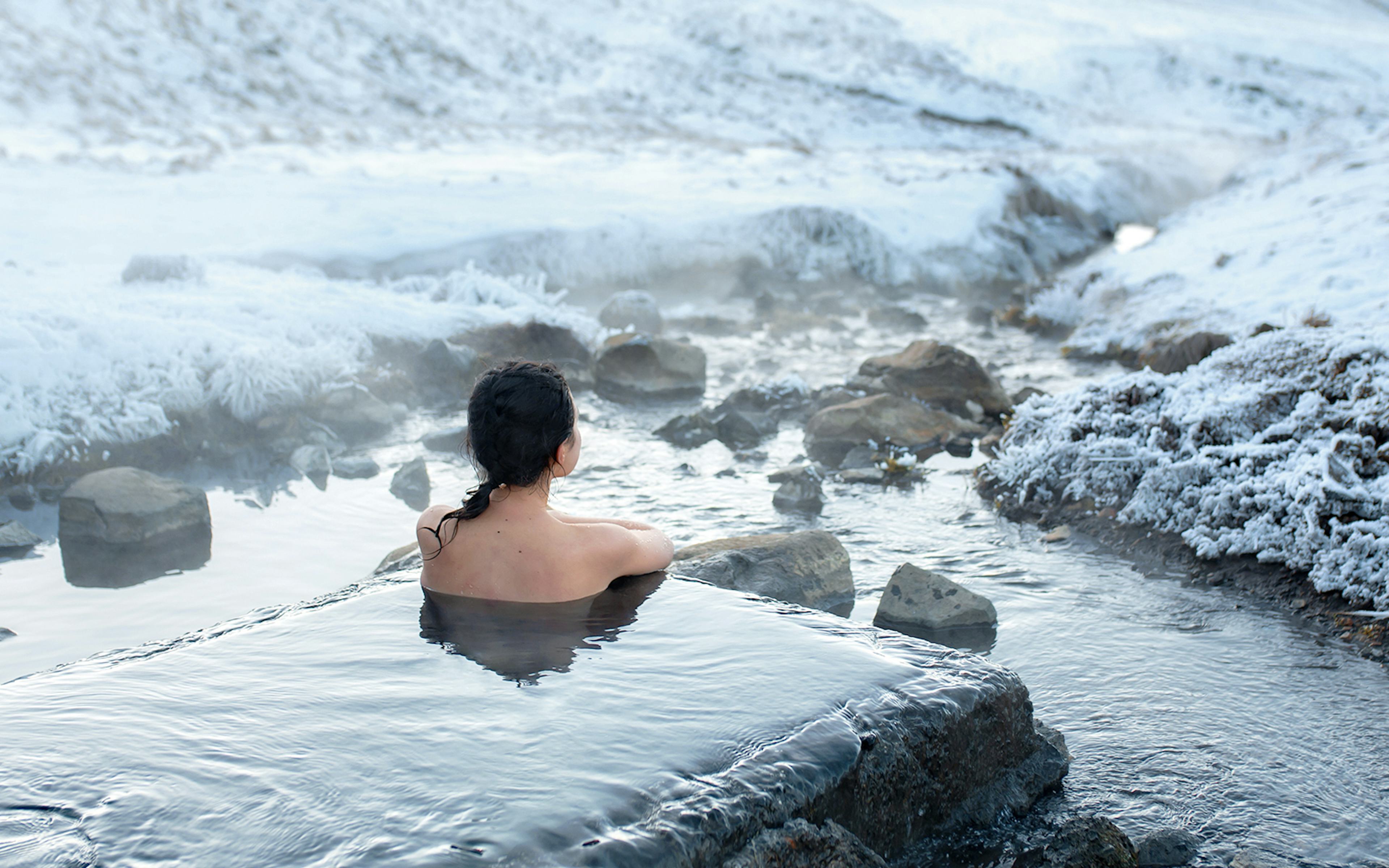 Visitor relaxing in a geothermal spa surrounded by snowy landscape, Iceland.