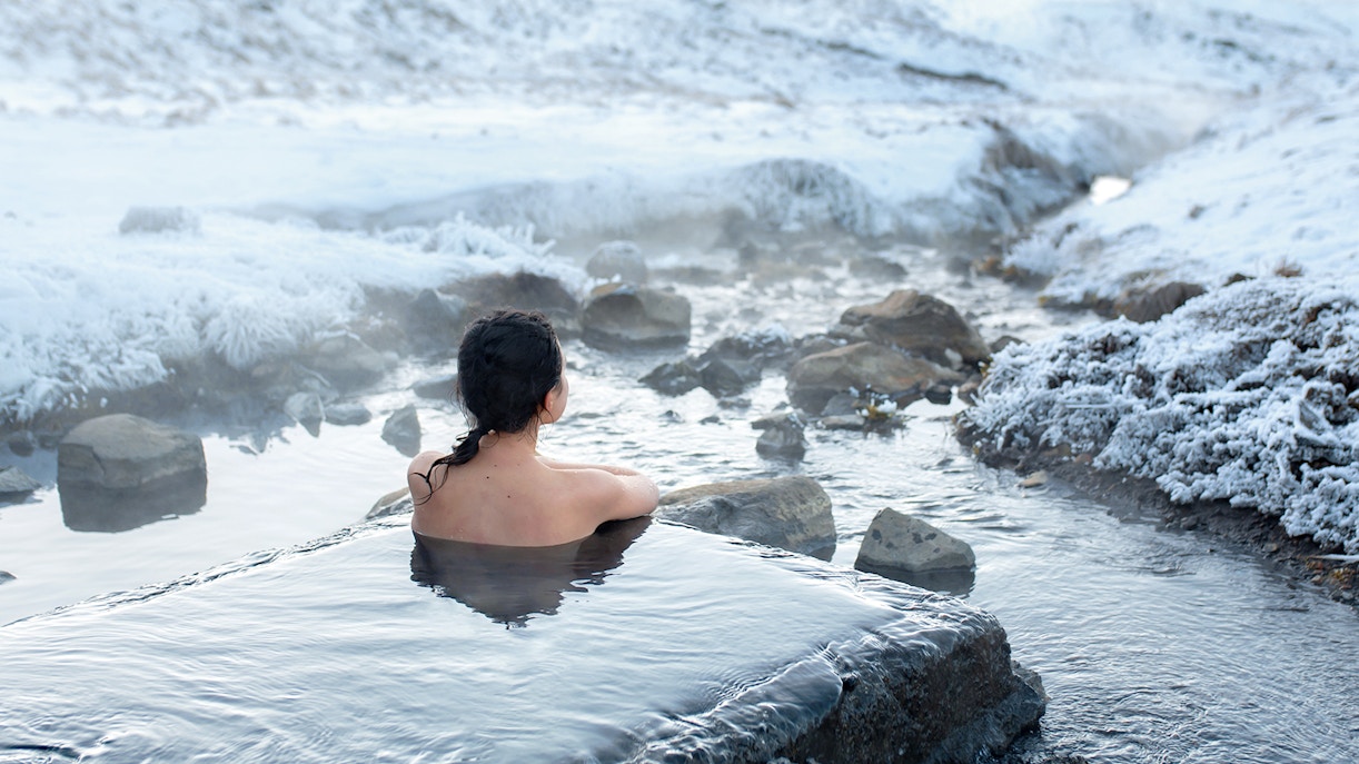 Visitor relaxing in a geothermal spa surrounded by snowy landscape, Iceland.