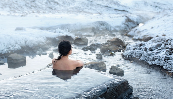 Visitor relaxing in a geothermal spa surrounded by snowy landscape, Iceland.