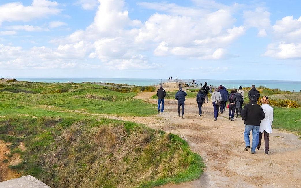 Tour group walking along Normandy beach cliffs with ocean view.