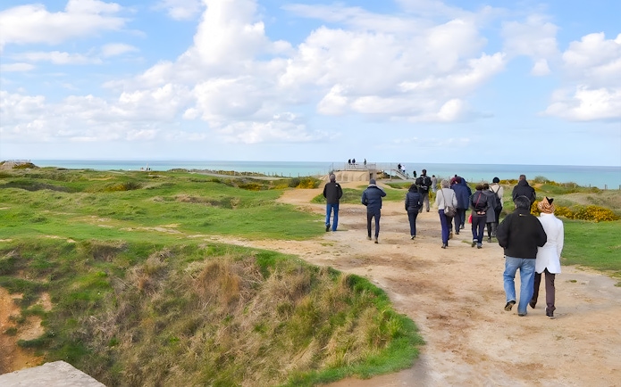 Tour group walking along Normandy beach cliffs with ocean view.