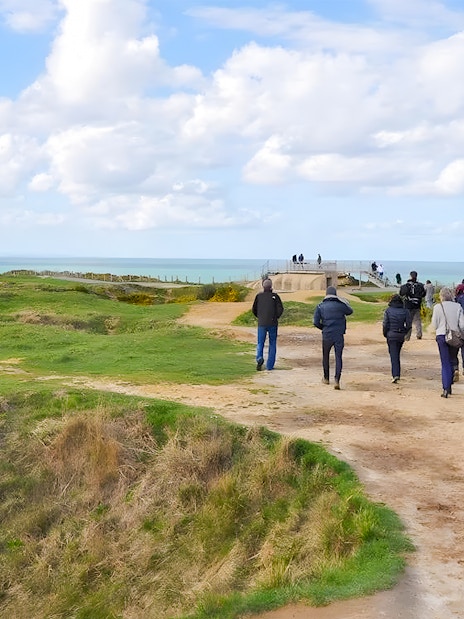 Tour group walking along Normandy beach cliffs with ocean view.