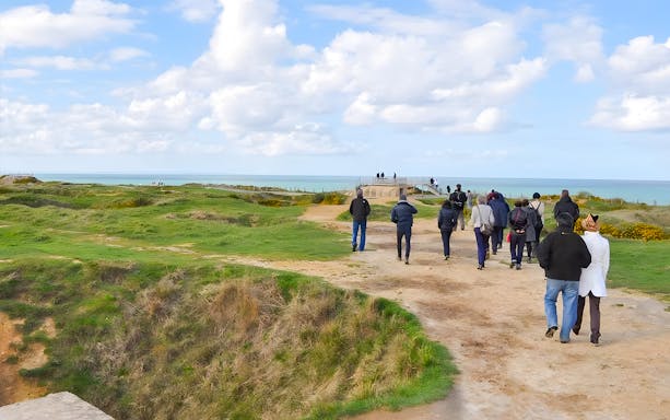 Tour group walking along Normandy beach cliffs with ocean view.