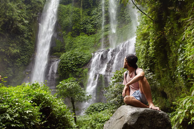 Person sitting on rock admiring lush waterfall in Chiang Mai, Thailand.