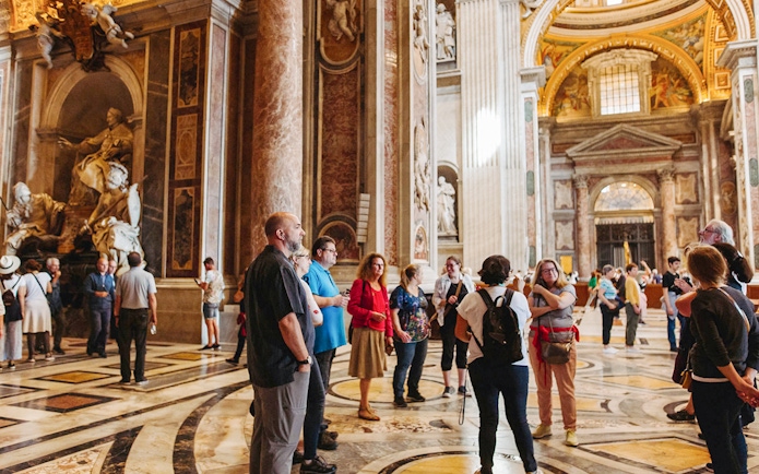 Tour group with guide inside St. Peter’s Basilica, Rome, near ornate sculptures.