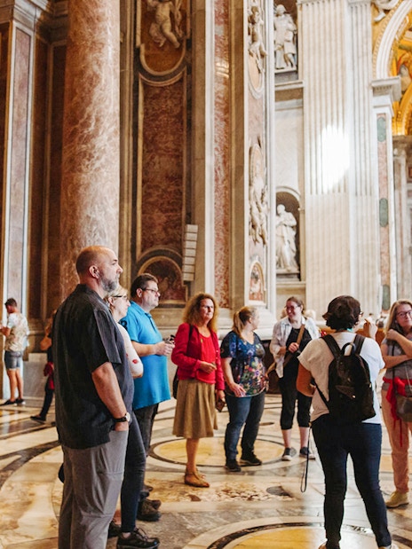 Tour group with guide inside St. Peter’s Basilica, Rome, near ornate sculptures.