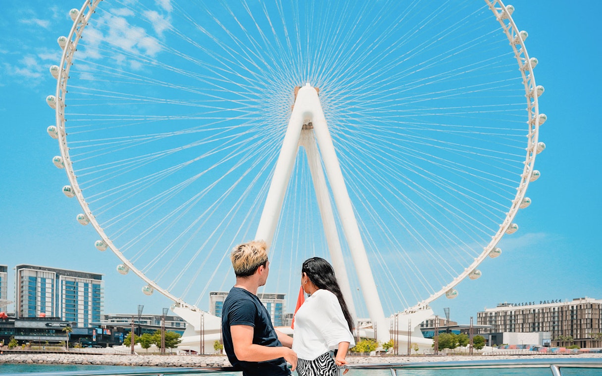 Couple viewing Ain Dubai Ferris wheel from waterfront.