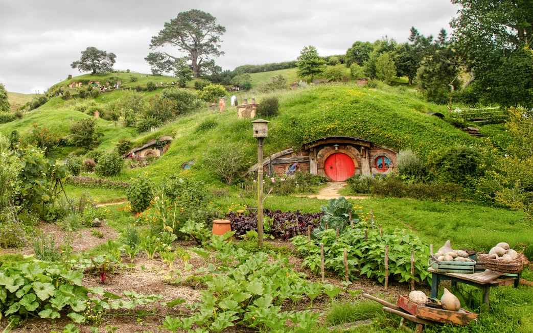 Panoramic view of Hobbiton movie set with lush green hills and iconic round door.