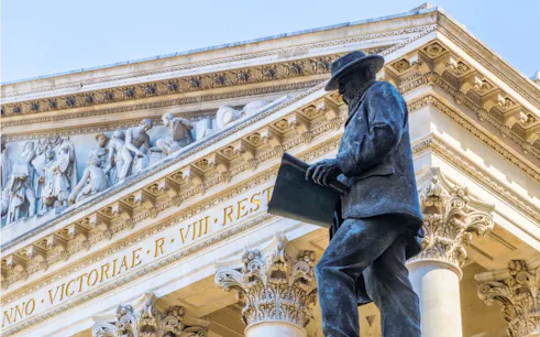 Statue of a man reading a book in front of a historic building in London.