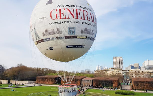 Ballon de Paris Generali tethered in a park with cityscape in the background.