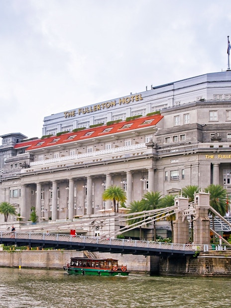 Fullerton Hotel in Singapore with a view of the river and nearby bridge.