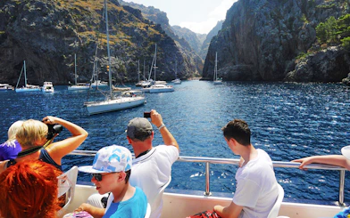 Tourists on a boat in Mallorca, capturing views of sailboats and rocky cliffs.