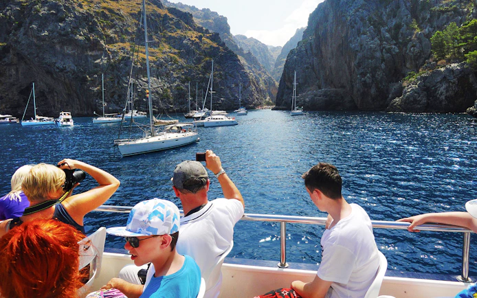 Tourists on a boat in Mallorca, capturing views of sailboats and rocky cliffs.