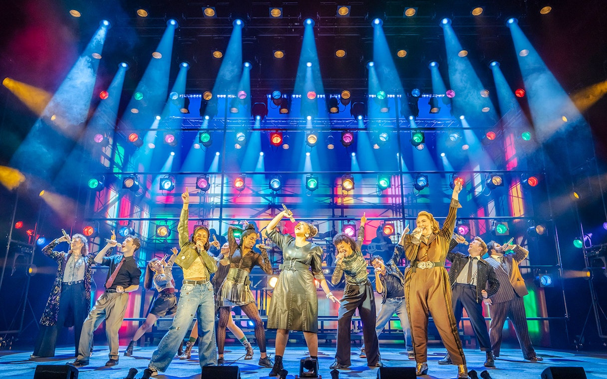 Performers singing on stage under colorful lights at Just for One Day event.